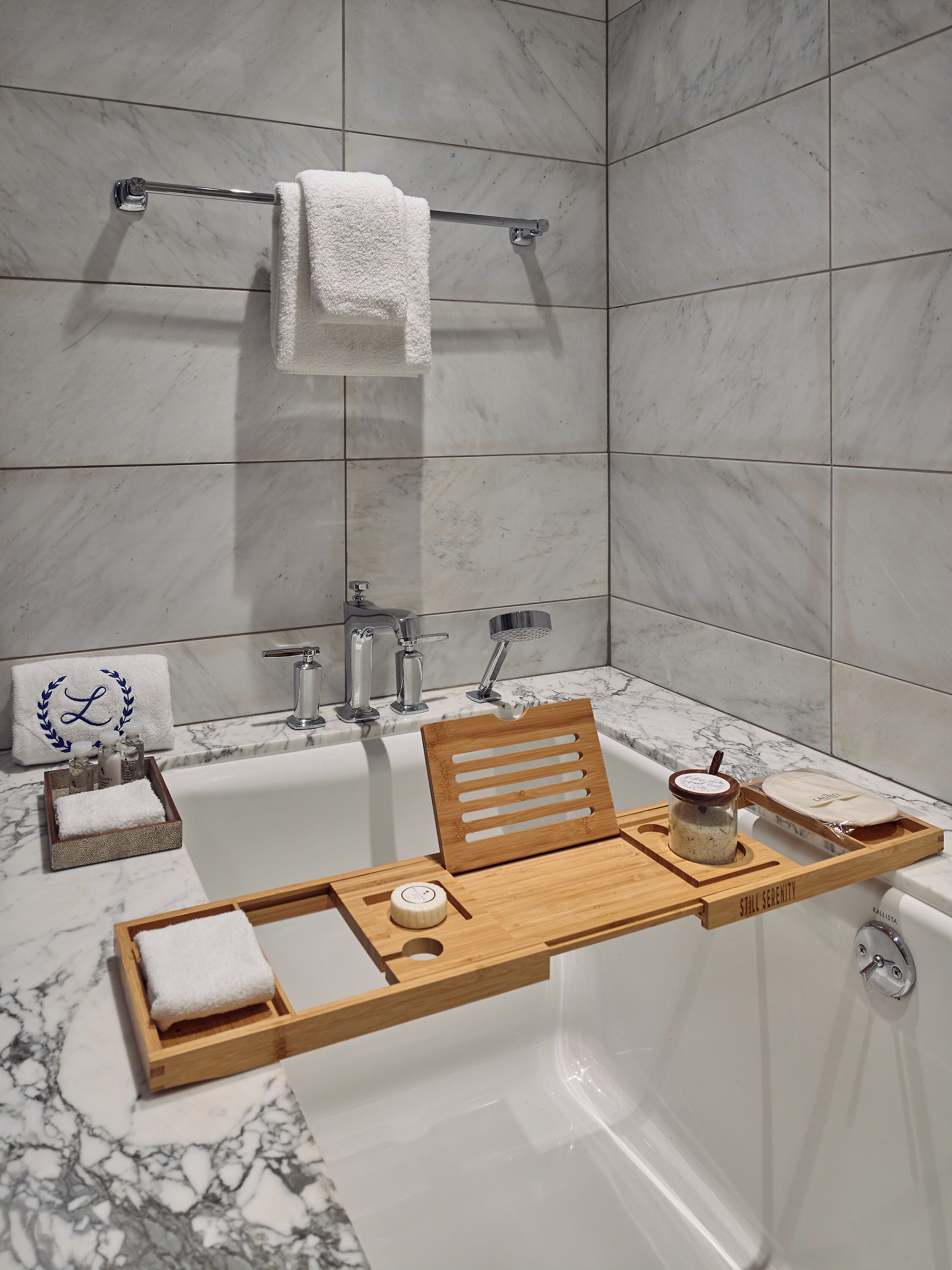 A modern bathroom with a marble sink, a wooden tray with toiletries, and a towel rack.