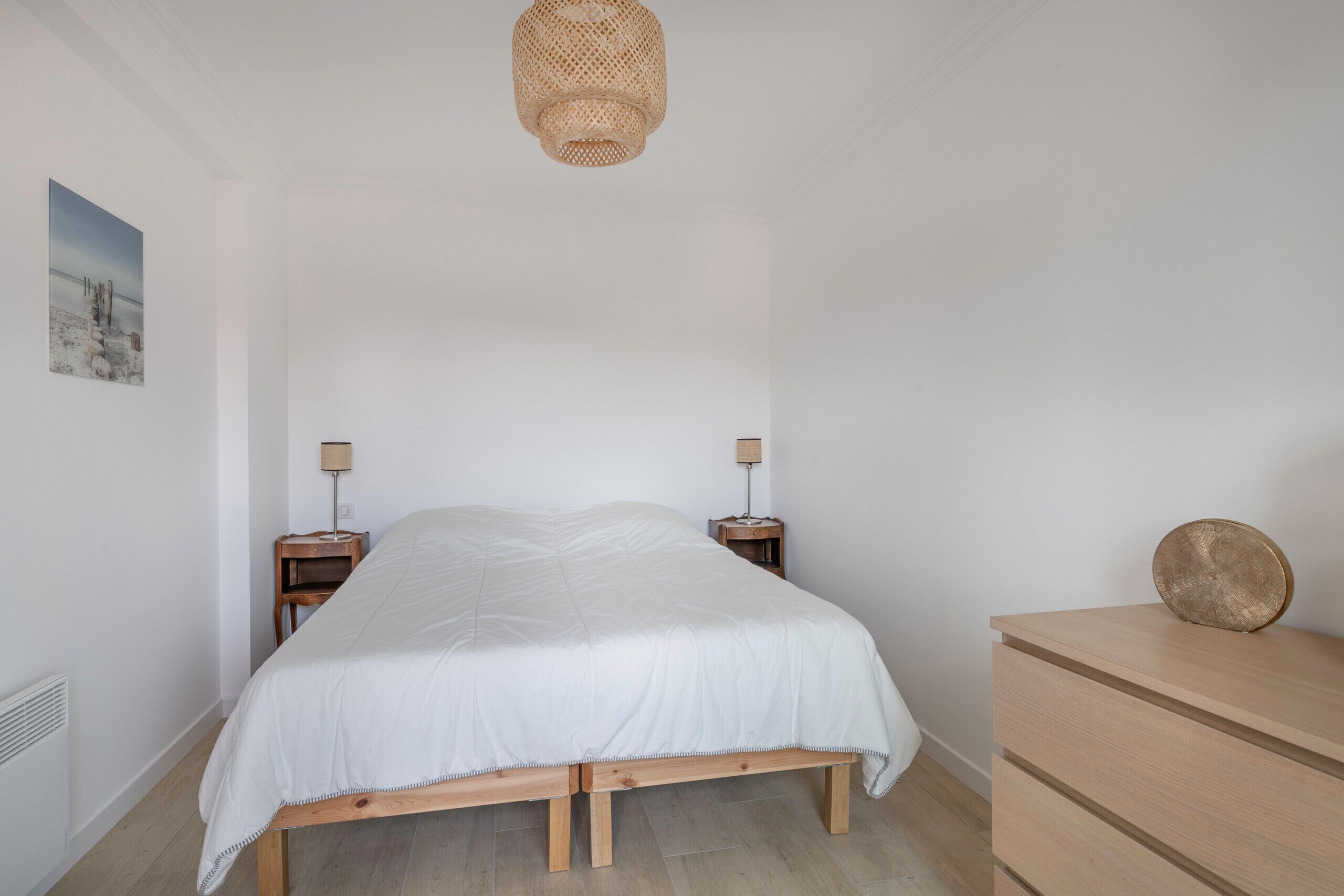 Un dormitorio con una cama, dos mesitas de noche, un aparador y una lámpara colgante.