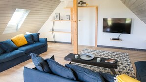 Uma sala de estar moderna com um sofá azul, uma mesa de centro de madeira e uma TV fixada na parede.