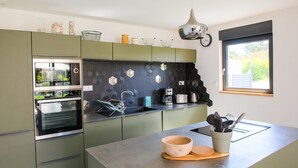 Uma cozinha moderna com armários verdes, forno de aço inoxidável, cafeteira e janela com vista para vegetação.