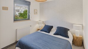 Quarto com cama grande, duas luminárias de cabeceira, janela com vista para vegetação e parede texturizada.