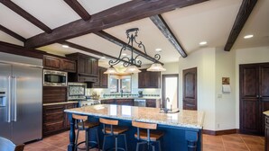 A spacious kitchen with dark wood cabinets, a stainless steel refrigerator, a large island with bar stools, and a hanging light fixture. - Stunning 3 bed/2.5 bath Mediterranean Villa with FABULOUS Ocean Views! (Cambria)