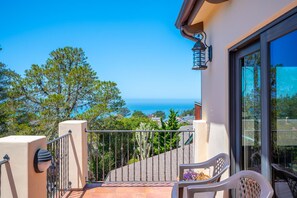 A balcony with a view of the sea, a chair, and a lamp.