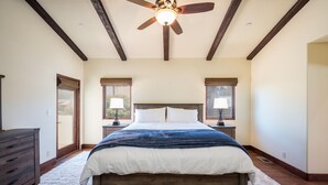 A bedroom with a large bed, wooden ceiling beams, two bedside lamps, and a ceiling fan. - Stunning 3 bed/2.5 bath Mediterranean Villa with FABULOUS Ocean Views! (Cambria)
