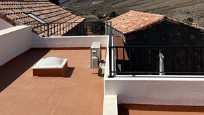 A rooftop terrace with terracotta tiles, a white wall, and a view of a mountainous landscape.