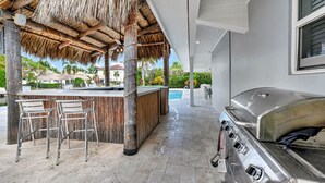 A covered outdoor area with a grill, bar, and chairs near a pool. - 943 Managed by Brampton Park (Delray Beach)