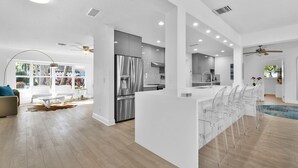 A modern kitchen with a stainless steel refrigerator, a dining area with clear chairs, and a large window offering a view of the outdoors. - 943 Managed by Brampton Park (Delray Beach)