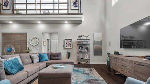 A spacious living room with a large sectional sofa, a coffee table, and a TV mounted on the wall. - Fayetteview Rooftop Balcony Hot Tub 5 Min to DT (Fayetteville)
