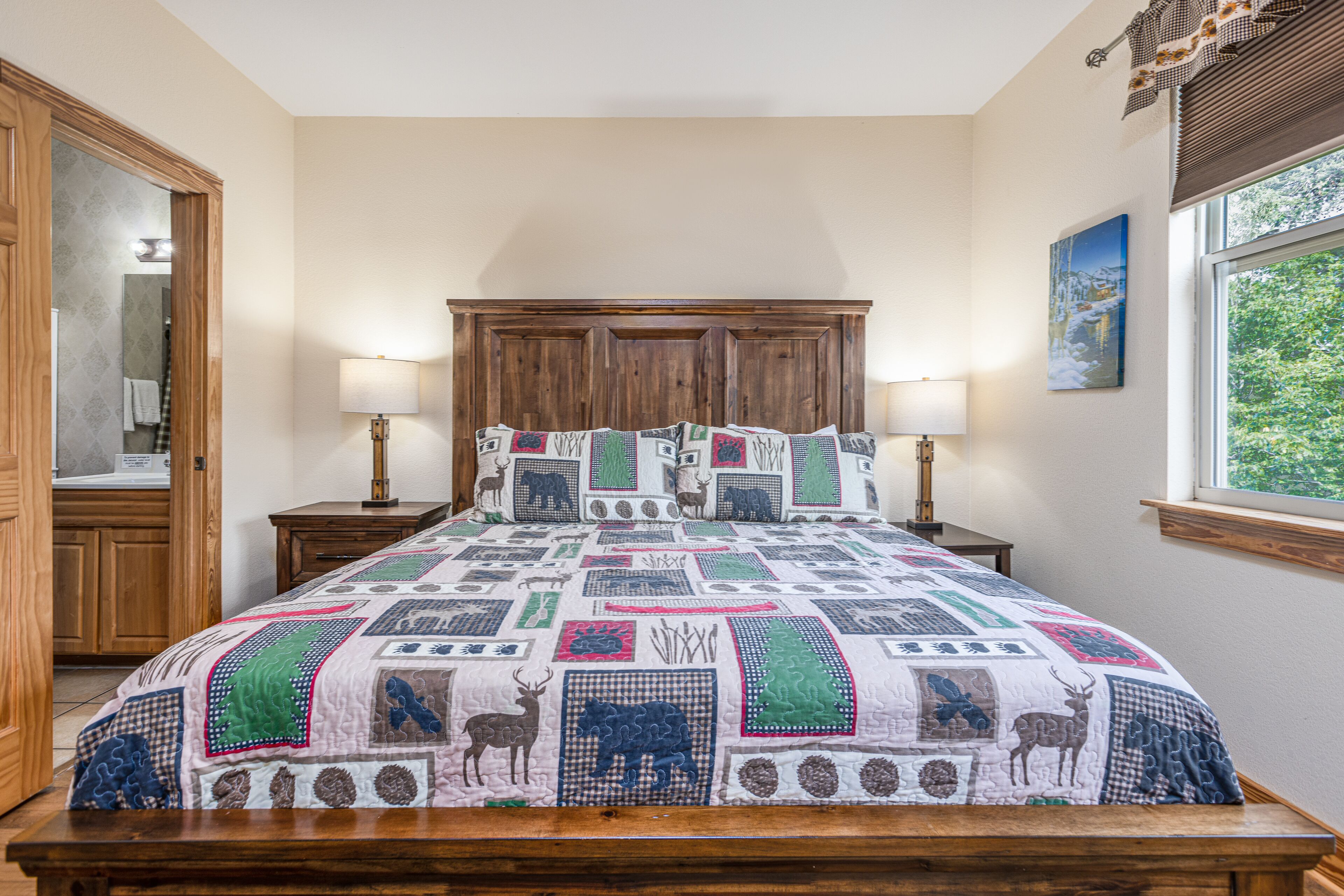 A bedroom with a large bed, wooden headboard, two bedside tables with lamps, a mirror, and a window with a view of greenery.