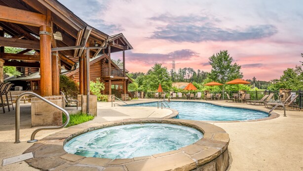 A wooden cabin with a hot tub and a pool, surrounded by outdoor seating and a fence.