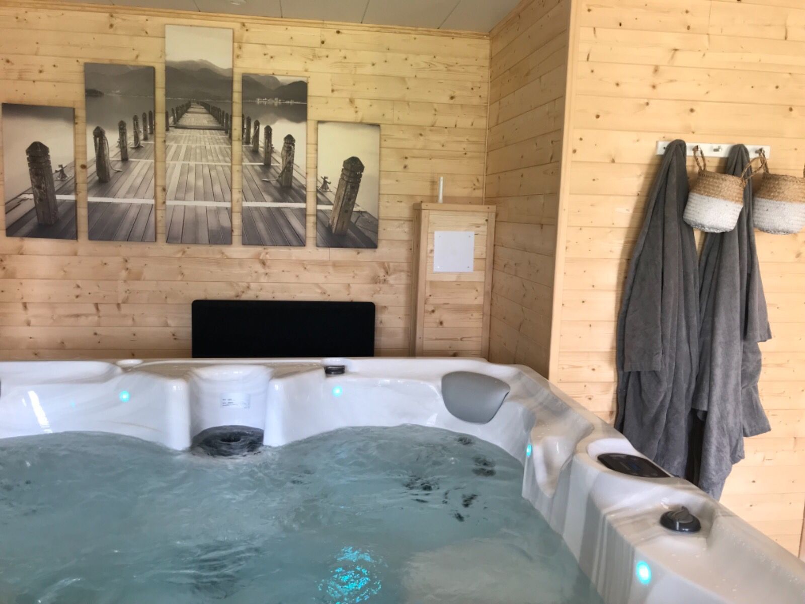 Habitación de cabaña de madera con un jacuzzi, paredes de madera y tres cuadros con imágenes de un puente.