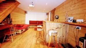 A wooden interior with a staircase, a bar area, and a seating area with red cushions.
