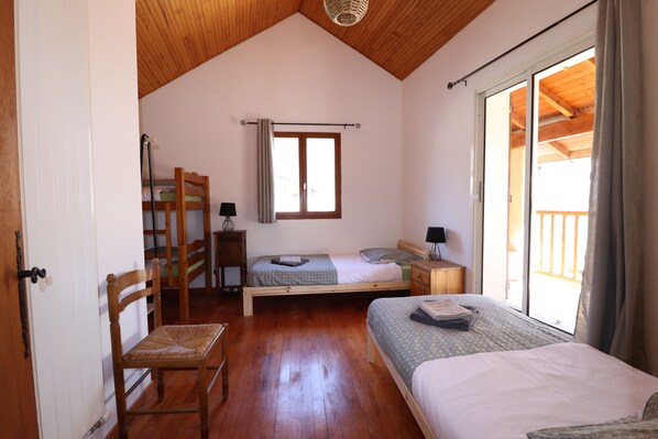 A bedroom with two beds, wooden flooring, a window with curtains, and a view of the outside balcony. - Spacious house in the heart of the Colmars ramparts! (Colmars)