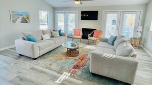 A spacious living room with a white sofa set, a coffee table, and two armchairs. A flat-screen TV is mounted on the wall, and there is a fireplace. - Cozy 3BR Townhome w/ Free Beach Service & Golf (Destin)