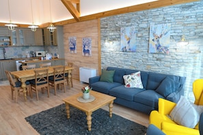 A living room with a blue sofa, yellow armchair, wooden dining table, and a stone wall with deer paintings. - Villa Letizia near Pirin Golf Resort (Razlog)