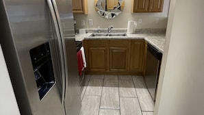 A modern kitchen with a stainless steel refrigerator, wooden cabinets, a granite countertop, and a patterned backsplash. - Cute Townhouse in Cherokee Village where adventures await! (Cherokee Village)