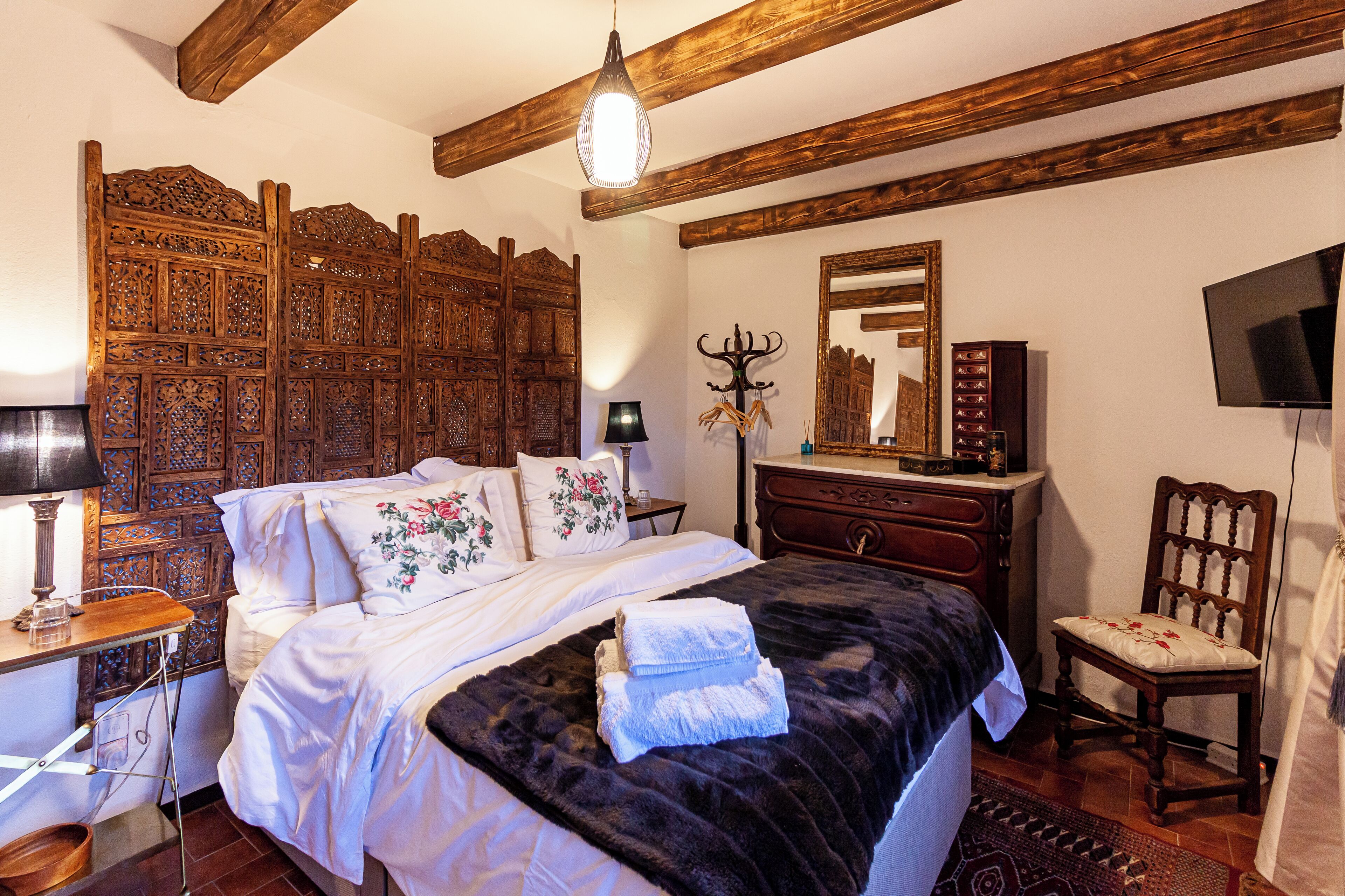 A bedroom with a large bed, wooden headboard, a dresser, a chair, a television, and a mirror.