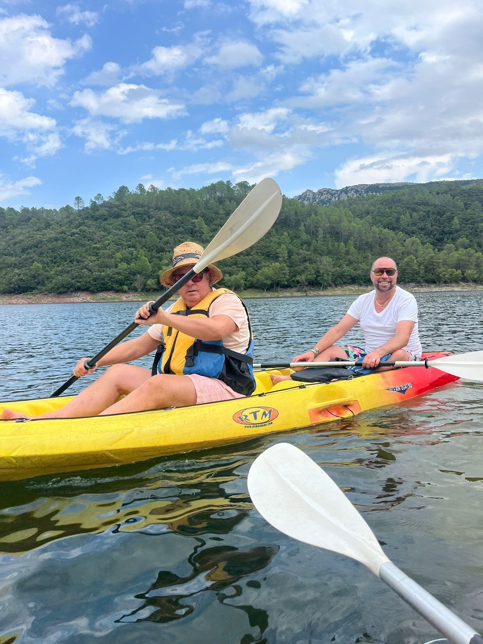 Due persone che fanno kayak su un lago calmo, con una collina boscosa sullo sfondo.