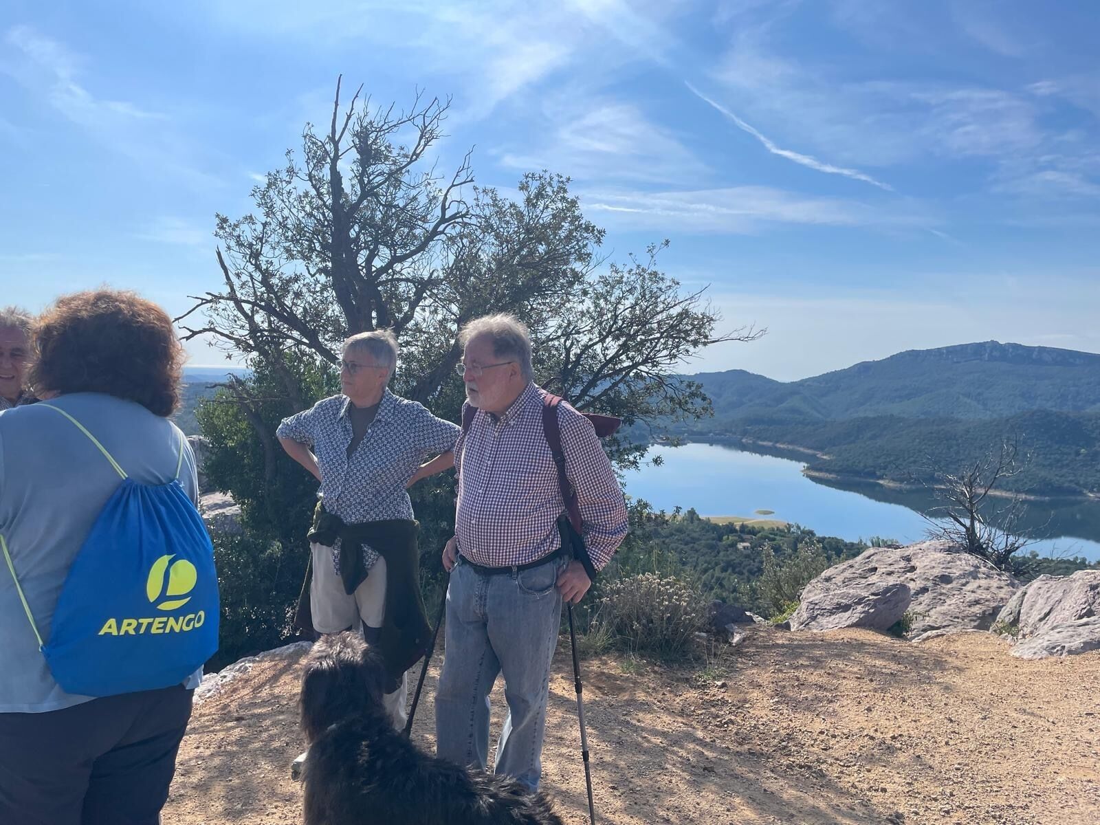 Un groupe de personnes se tient sur un sentier rocheux, avec une vue sur un lac et des montagnes en arrière-plan.