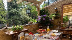 An outdoor dining area with a table set for breakfast, surrounded by greenery and rustic decor. - Masia Mimosa (Darnius)
