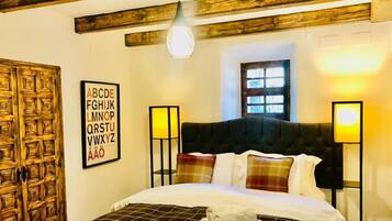 Una habitación de hotel con una cama grande, vigas de madera en el techo, una ventana y lámparas fijadas a la pared.