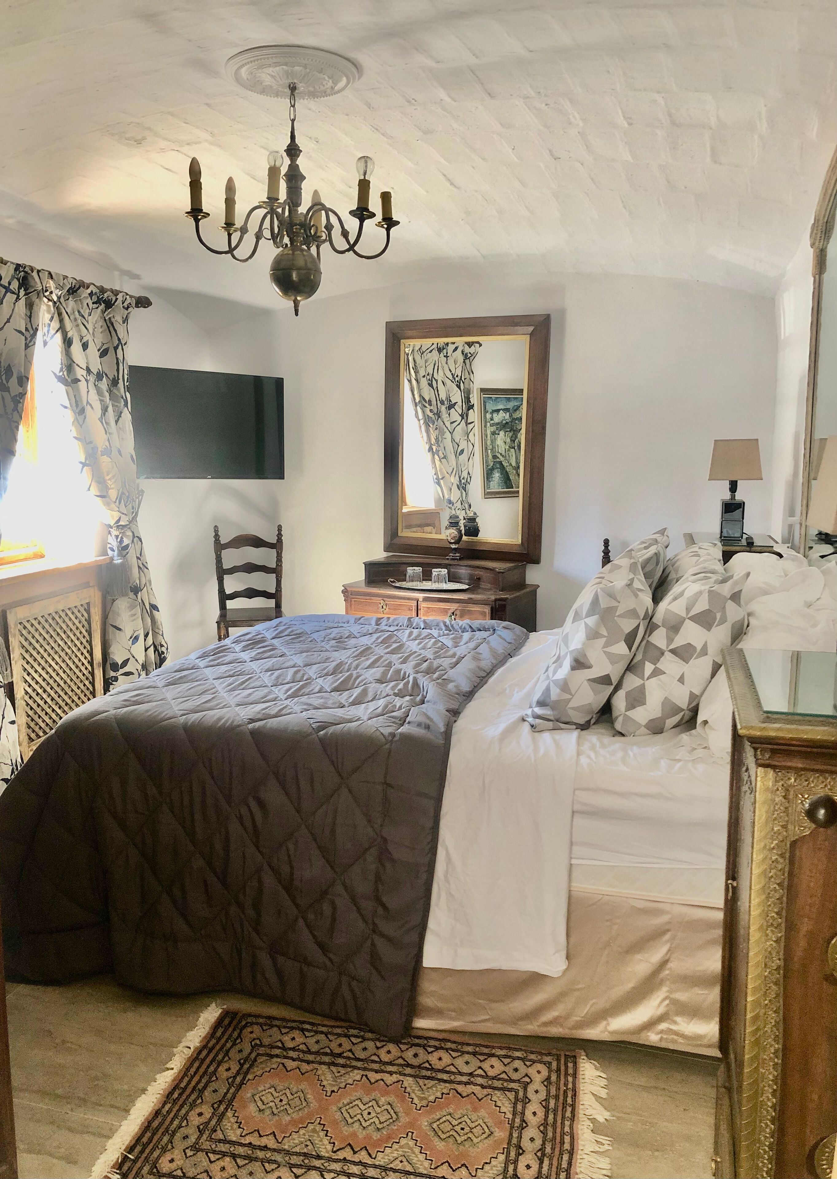 Een slaapkamer met een groot bed, een kroonluchter, een kaptafel, een spiegel en een televisie aan de muur.