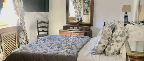 A bedroom with a large bed, a chandelier, a dresser, a mirror, and a television on the wall.