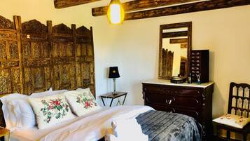 Un dormitorio con cama, cabecera de madera, cómoda, silla, lámpara y espejo.