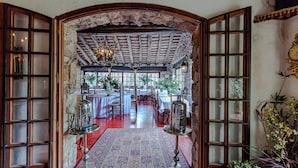 An open archway leading to a dining area with tables, chairs, and a chandelier. - Masia Mimosa (Darnius)