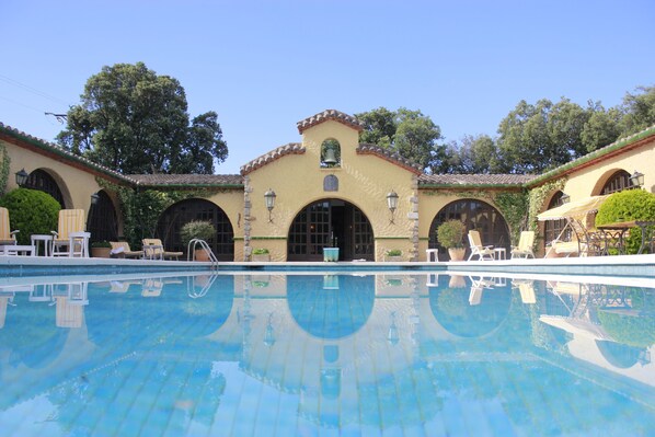 A pool area with lounge chairs and a building with arched windows and a bell.