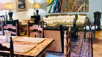 Un área de comedor con una mesa y sillas de madera, un conjunto de sofás y un cuadro abstracto y colorido en la pared.