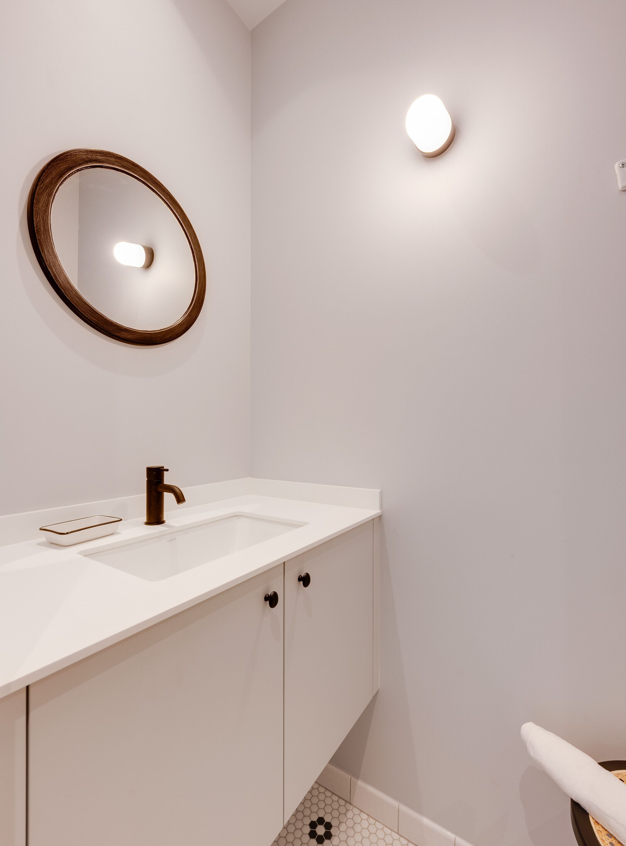 Une salle de bain moderne avec un meuble-lavabo blanc, un miroir rond, un simple lavabo et des toilettes.