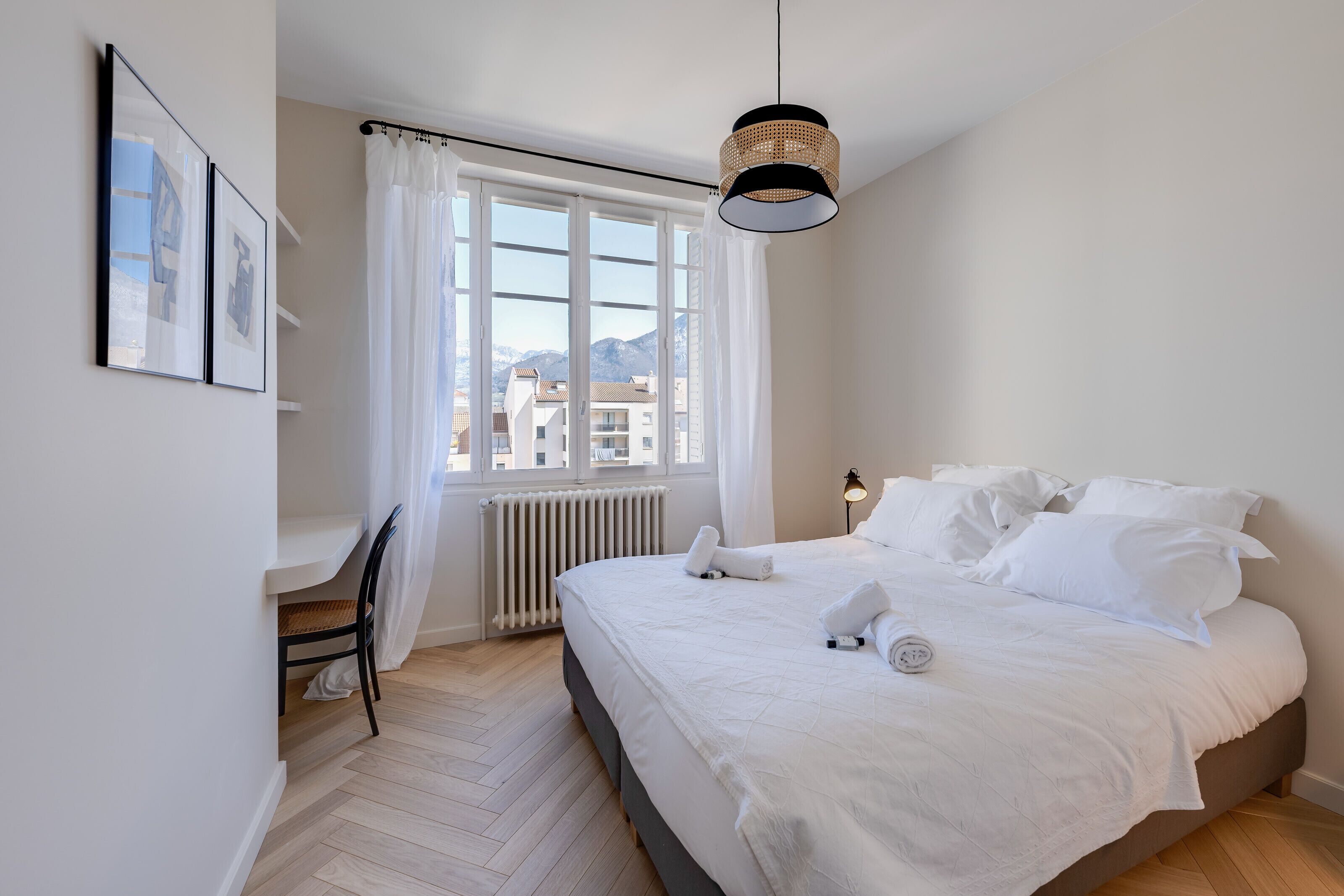 Et soveværelse med en stor seng, en stol, et vindue med gardiner og en hængende lampe.
