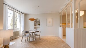 A modern dining area with a wooden herringbone floor, white walls, and a dining table set with chairs.
