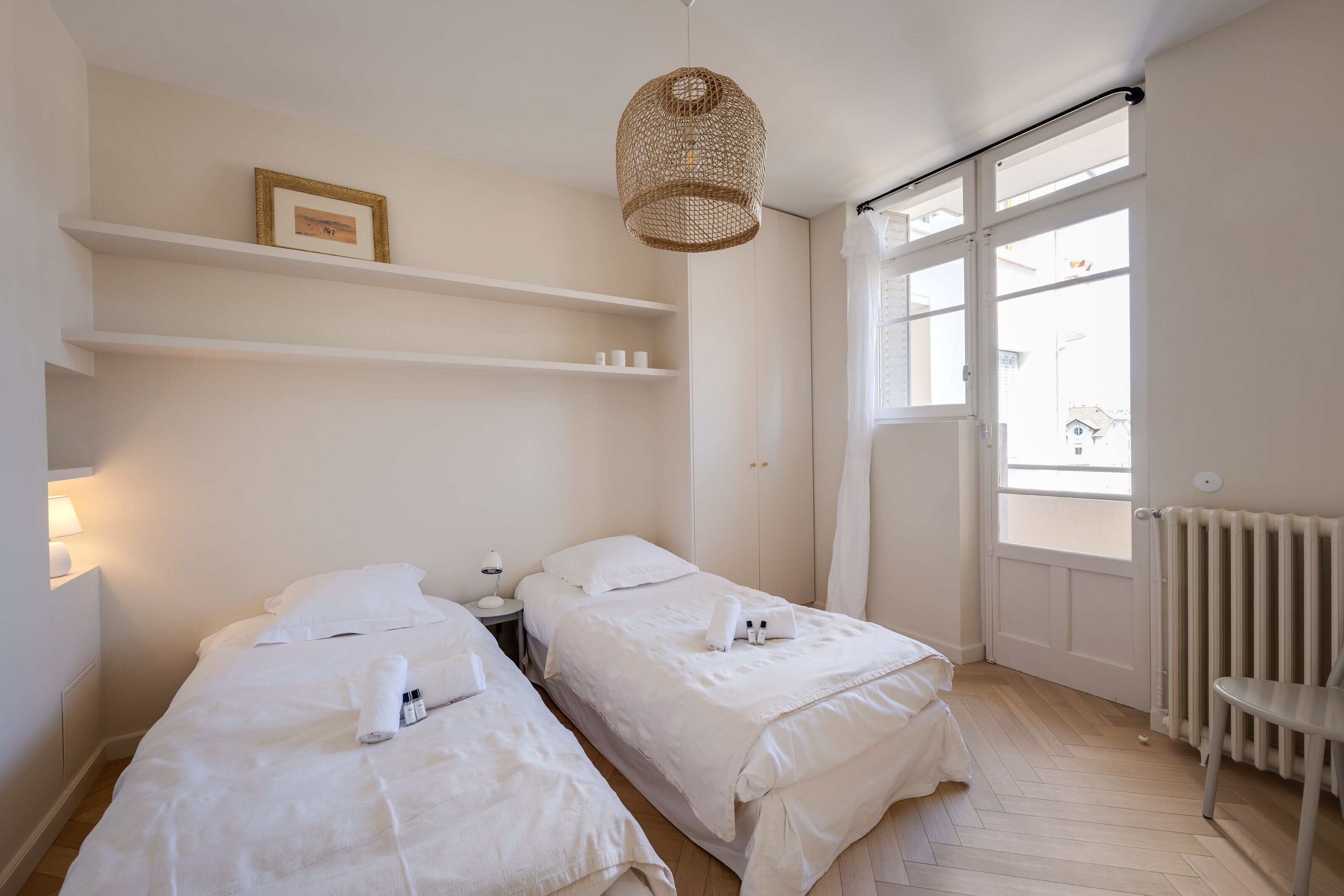 Een hotelkamer met twee bedden, een groot raam, een radiator en een hanglamp.
