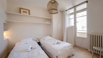 Een hotelkamer met twee bedden, een groot raam, een radiator en een hanglamp.