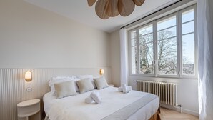 A modern bedroom with a large bed, bedside tables, a radiator, and a window with curtains.