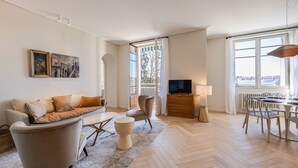 A modern living room with a sofa, armchairs, a coffee table, a TV, and a dining area with chairs and a table.