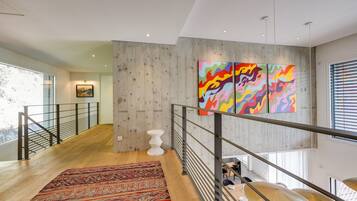 Un intérieur moderne avec un plancher en bois, un tapis à motifs, un escalier avec des rampes en métal et une peinture abstraite aux couleurs vives accrochée au mur.