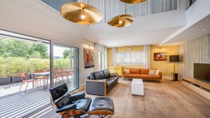 Una sala de estar moderna con un televisor grande, sofás de cuero y una zona de comedor con sillas anaranjadas.