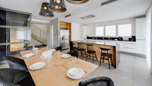 Una cocina moderna con una isla central, un comedor con mesa de madera dispuesta para cuatro personas, y una escalera que conduce a un nivel superior.