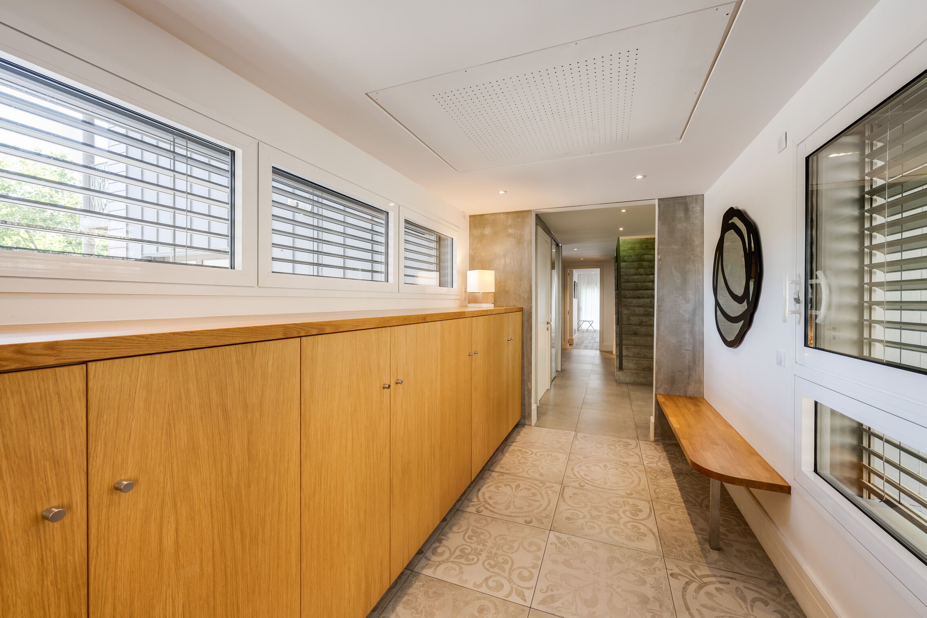 A modern kitchen with wooden cabinets, a bench, and large windows with blinds.