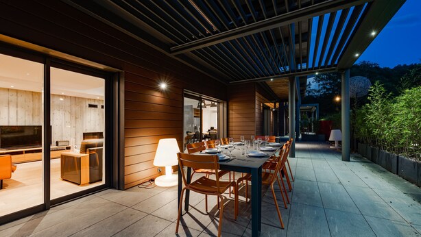 Un área de comedor al aire libre con una mesa dispuesta para seis personas, rodeada de sillas de madera.
