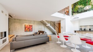 A modern living room with a grey sofa, white chairs, and a staircase leading to a kitchen area.