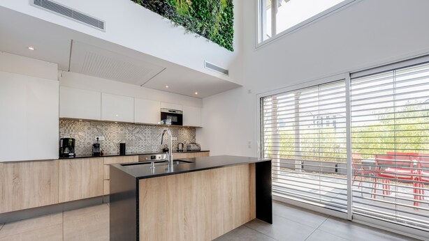 A modern kitchen with a large island, built-in appliances, and a view through large windows.