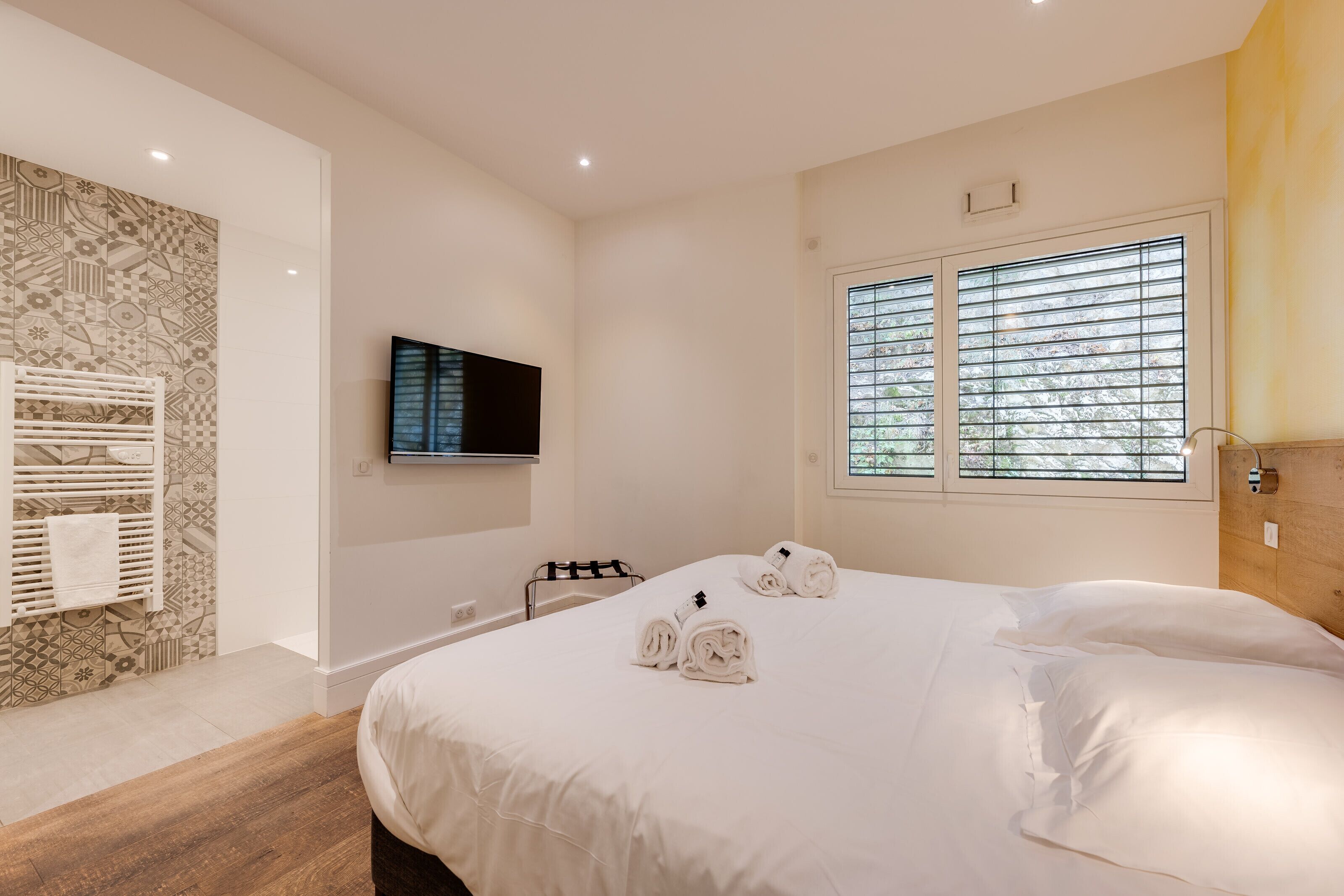 Ein Hotelzimmer mit einem großen Bett, einem an der Wand montierten Fernseher und einem Fenster mit Jalousien.