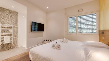 Ein Hotelzimmer mit einem großen Bett, einem an der Wand montierten Fernseher und einem Fenster mit Jalousien.