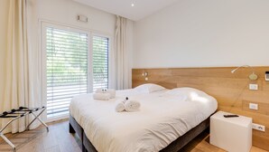 A neatly made bed with white linens and towels, a wooden headboard, and a bedside table with a remote control.