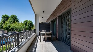 A balcony with a table and chairs, a view of parked cars, and a building with horizontal siding.