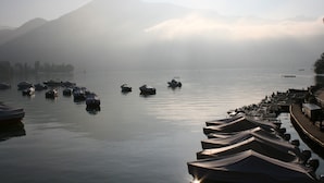 A calm lake with boats and a misty mountain backdrop.